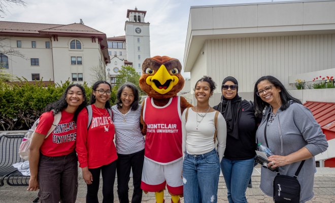 A family taking a group picture with the mascot, Rocky the Red Hawk