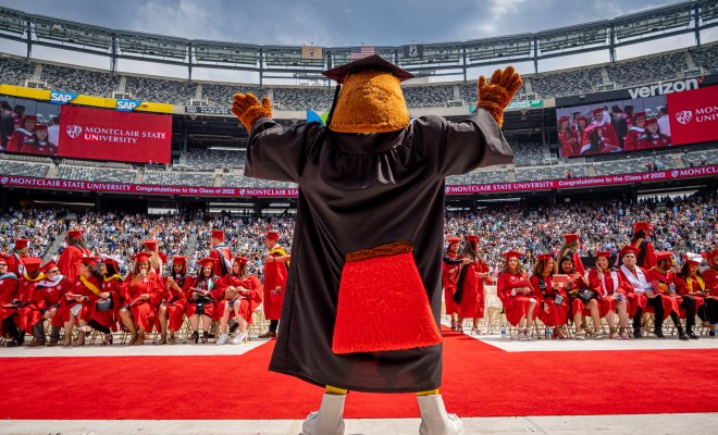 rocky the mascot standing on stage at commencement ceremony facing the crowd of graduating students and guest.