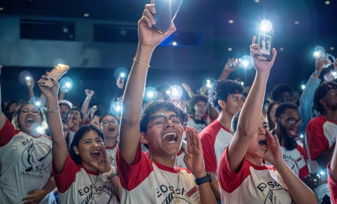 students in a crowd with their phone flashlights on.
