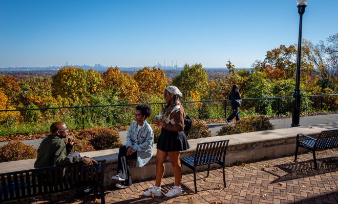 Students sitting outside on a bench overlooking the fall leaves. NYC in background.