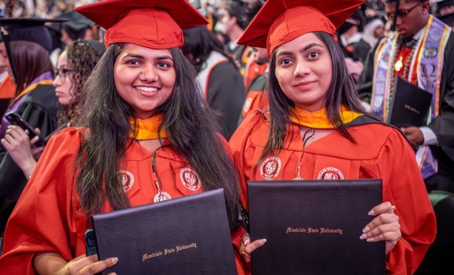 Two students holding their degrees while wearing their caps and gowns at a graduation ceremony 