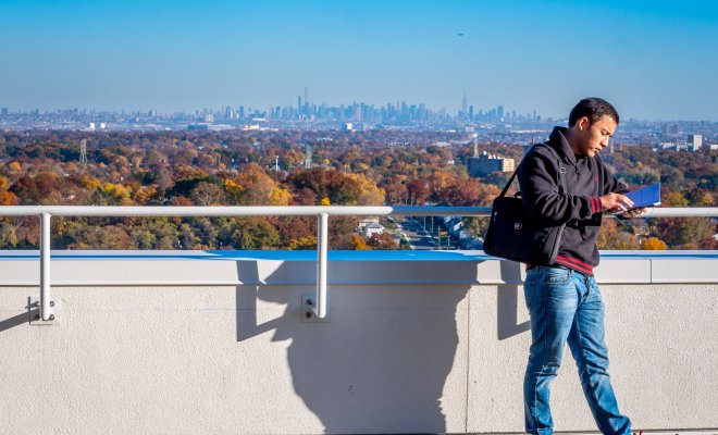 A student reads a book and leans against a wall overlooking North Jersey and New York City