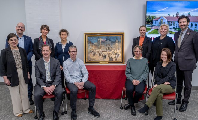 A group of people pose around a framed painting 