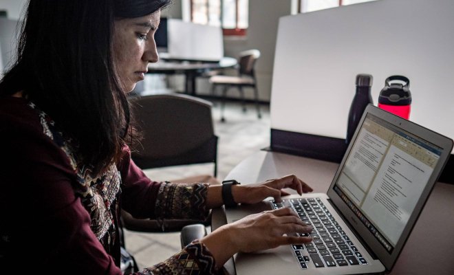 A college student types on a computer in a dark, empty classroom