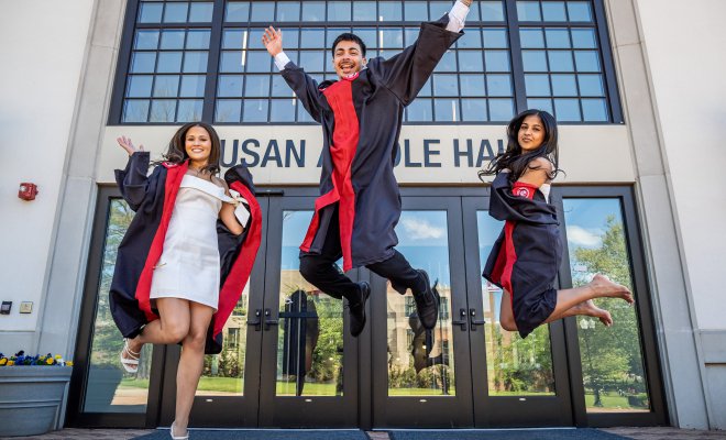 three graduates jumping outside on campus