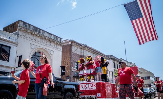 Individuals walking in parade procession around Montclair float, American flag above