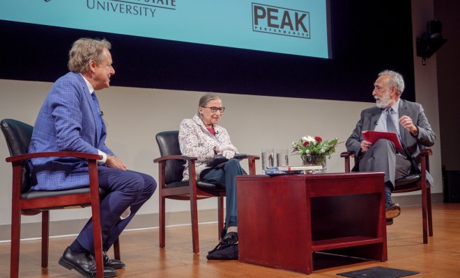 Ruth Bader Ginsburg on stage with two other men discussing.