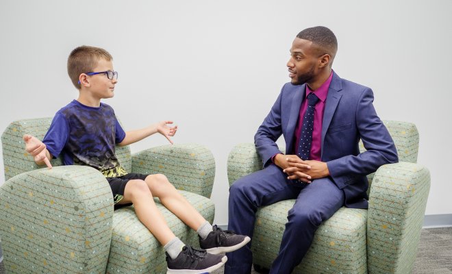A psychology student sits in a chair across from a child and speaks with him