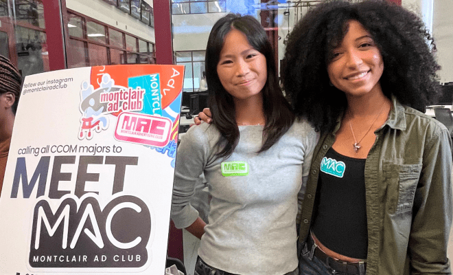 Two students pose in front a Meet Montclair Ad Club recruitment poster at the club fair.