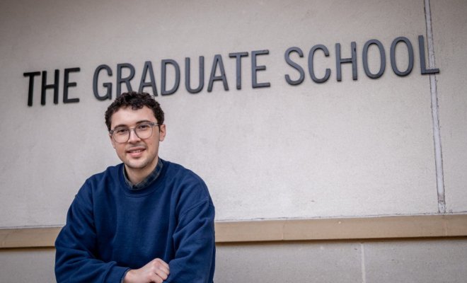 Student sitting in front of The Graduate School sign
