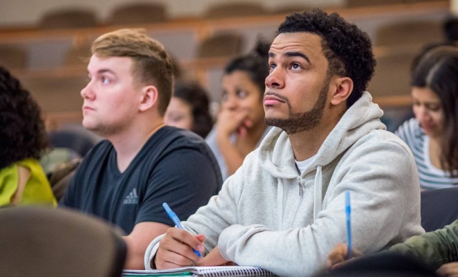 Two college students sitting in a classroom, taking notes during a lecture