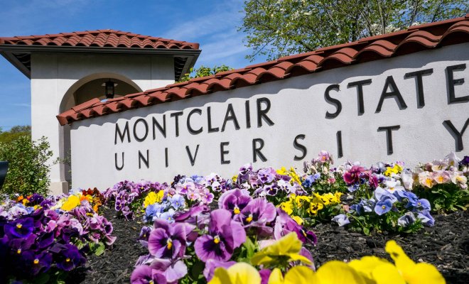 An exterior sign for Montclair State University with a bed of flowers in front of it