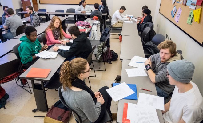 Groups of college students sit around a classroom discussing an assignment