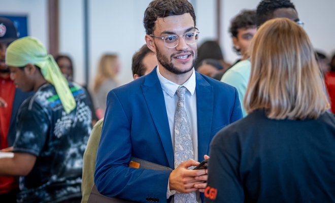 Student wearing a suit networks with an employer at a Career Fair.