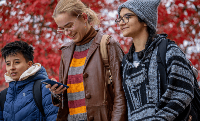 Three students walking together on campus in the fall.