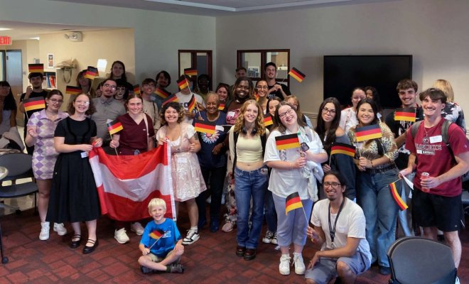 A large group of people stand together and hold small German flags while two people  hold a large Austrian flag