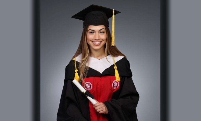 A woman poses in black cap and gown and holds a diploma