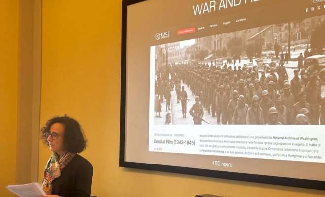 A college professor stands in front of a projector screen and delivers a presentation about "War and Film"