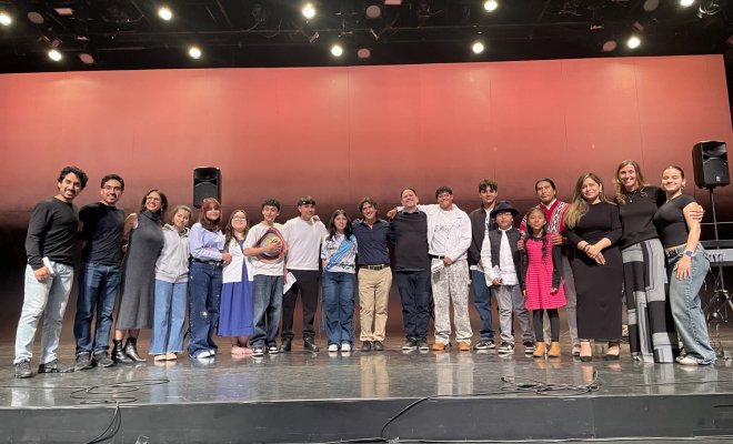 A group of college students and professors stand in a half-circle on a stage