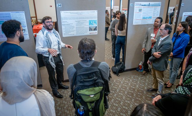 Student presenting his research poster to crowd. 