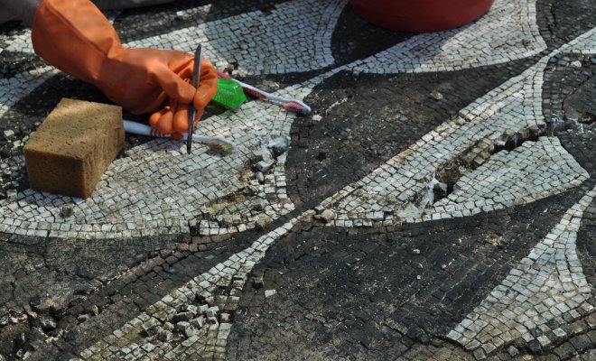 A hand holds a metal tool to clean a tile mosaic at an ancient Italian villa
