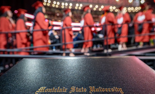 Diploma with graduates lined up on stage in background