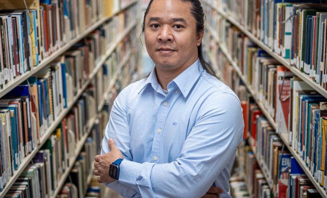 Kaung Hla Zan stands between two long shelves of books in a library.