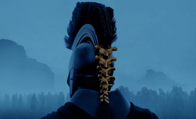 Man in helmet with gold spine on the back of his head riding into war. It is dark and foggy and you can see the outlines of the mountains ahead. 