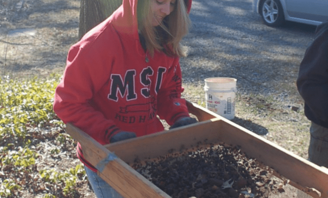 A woman in a Montclair State University University sweatshirt screens excavated soil