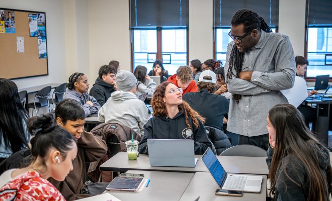Professor Jason Williams standing in class and talking to a student while the class works on group project