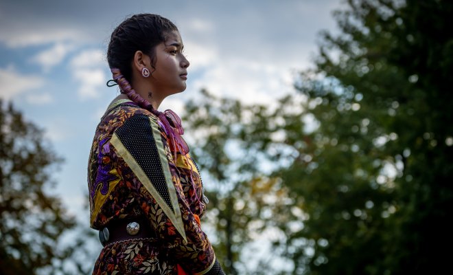 Indigenous tribal member standing with sky and trees in background