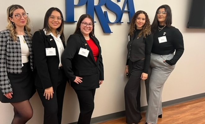 A group of five students standing and smiling with the letters P R S S A on the wall behind them.