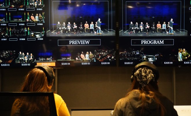Two people working on a TV production project, wearing headphones and looking at monitors, with their back to the shot.