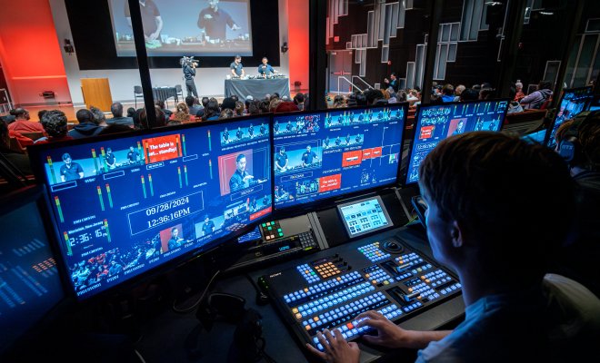 A student in front of several TV production monitors, controlling audio and visual elements of a show.