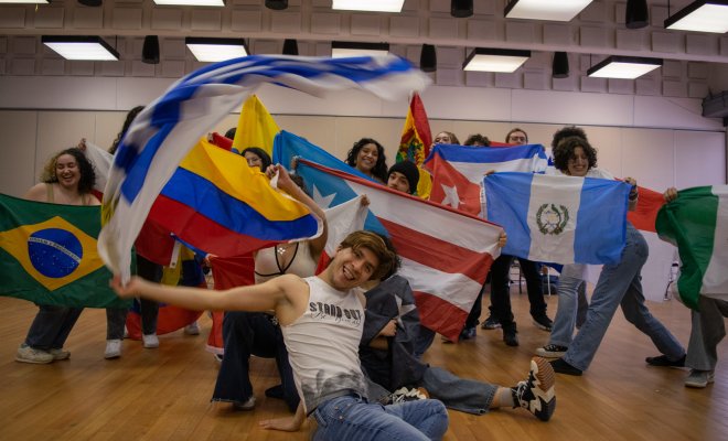 Students holding up flags from around the world, while smiling and standing and sitting in two rows.