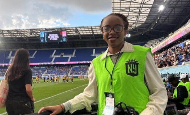Student in light green Gotham FC vest holding camera.