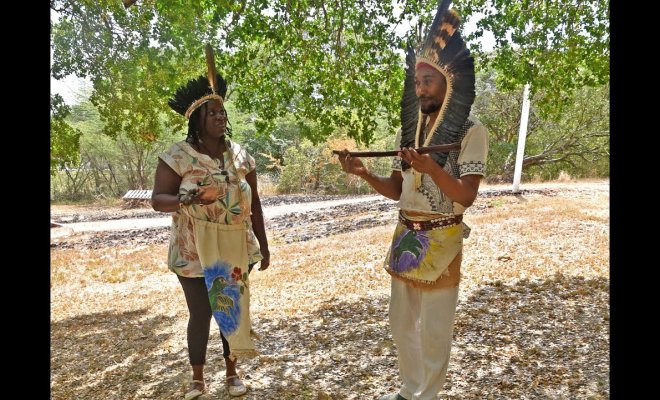 Two people wearing feathered ceremonial attire with ceremonial objects