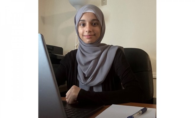 A person wearing a gray hijab works at a laptop while seated at a desk