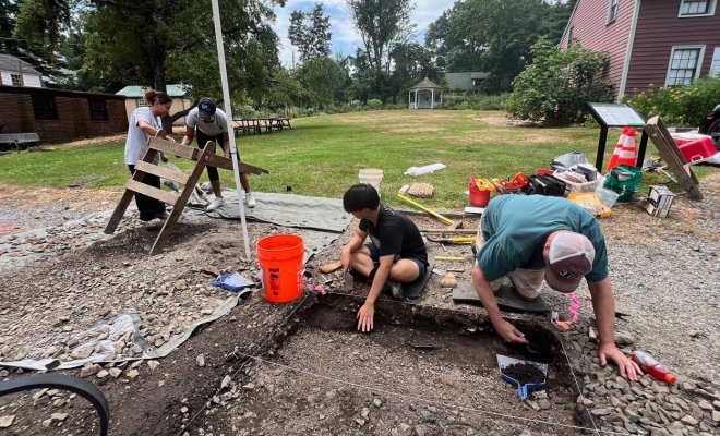 Two people kneel over a hole in the ground and sift through the soil
