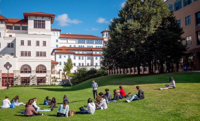 A college class sits on the lawn of a college campus