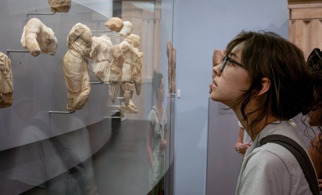 A college student looks at a museum display of small, broken marble statues