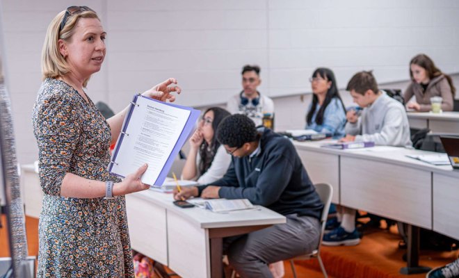 A college professor stands at the head of a class and delivers a lecture to students