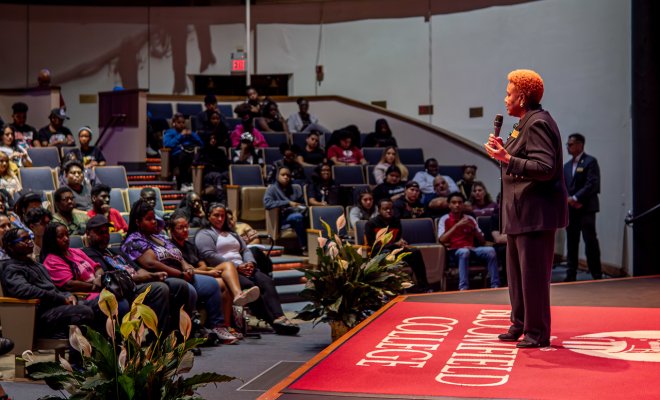 A speaker on a stage talking to a crowd of people 