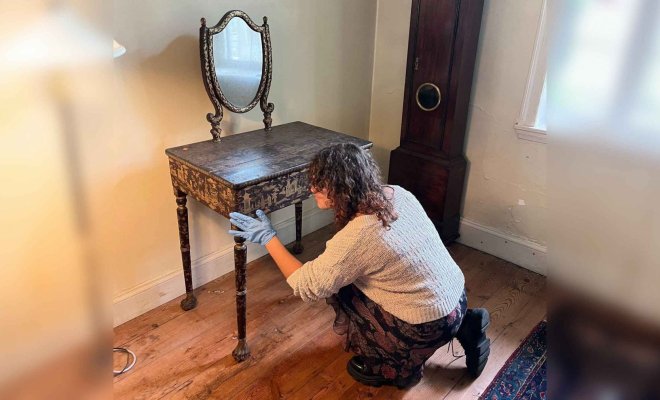 A person wearing gloves examines an old, wooden desk