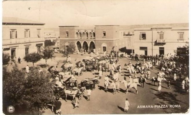 A sepia-toned image shows a busy town square in Asmara in Piazza Roma with horse-drawn carts, pedestrians, and surrounding buildings