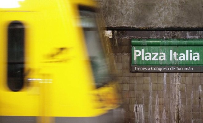 A yellow subway train moves through a station