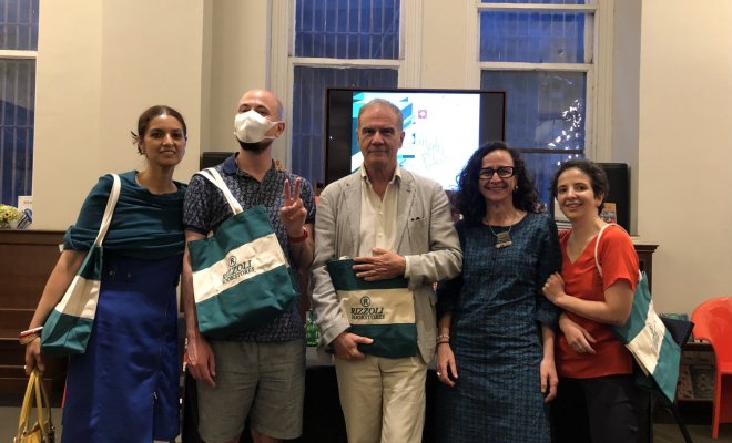 A group of people pose with tote bags in front of a small tv screen