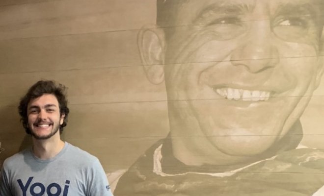 A college student stands in front of a wall decal of Yogi Berra from his playing days