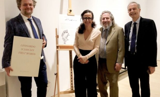 A group of people pose around an art piece on an easel, one of the people holds a large book