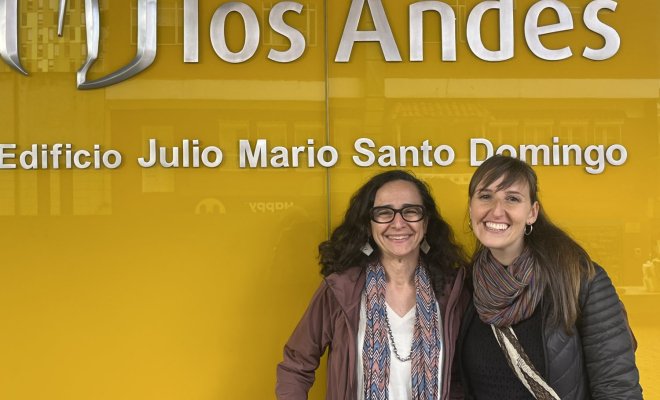 Two women pose in fornof a sign for the "Universidad de los Andes"